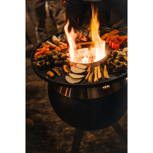 Höfats MOON 45 vuurkorf roestvrijstaal met hoge roestvrijstalen standaard. Voorzien van Geëmailleerd gietijzeren grillring en brandend vuur op een terras – rookvrije design vuurkorf met houtvergassingstechnologie