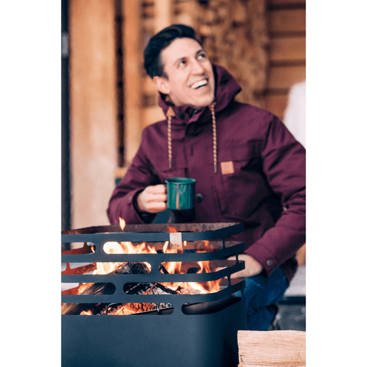Man geniet buiten van een warm vuur in de Höfats Cube vuurkorf van zwart roestvrij staal.