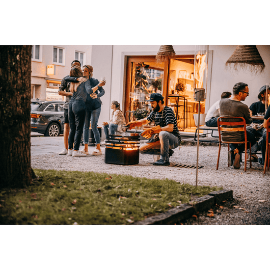 Zomerse setting met mensen die buiten genieten op een terras, waarbij de Höfats Cube als vuurkorf wordt gebruikt.