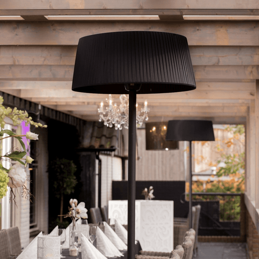 Zwarte staande heater onder houten veranda bij tuintafel.